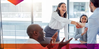 3 coworkers smiling, laughing, and shaking hands in a brightly lit office.